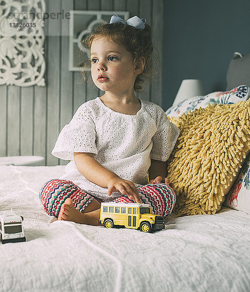 Nachdenkliches Mädchen mit Spielzeug auf dem Bett sitzend