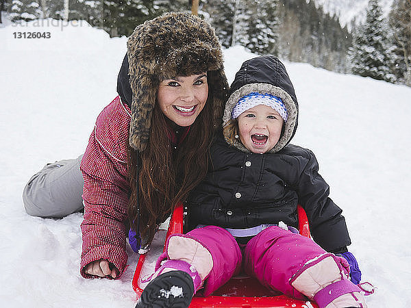 Porträt einer glücklichen Mutter mit Tochter auf schneebedecktem Feld sitzend