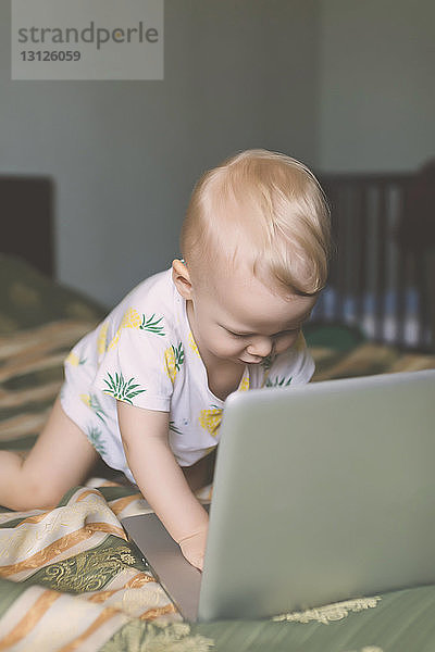 Süßer kleiner Junge benutzt Laptop-Computer im Bett zu Hause