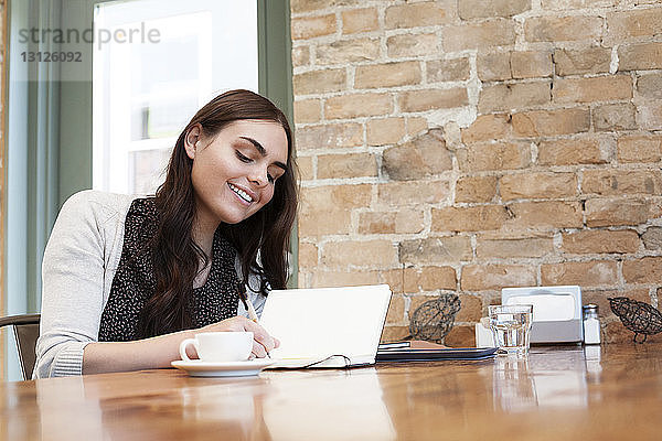 Frau schreibt in Tagebuch  während sie im Café sitzt