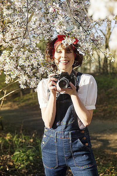 Porträt einer glücklichen Frau  die im Park stehend durch die Kamera fotografiert