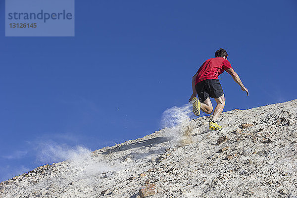 Tiefblick auf einen Mann  der auf einem Berg vor klarem  blauem Himmel joggt