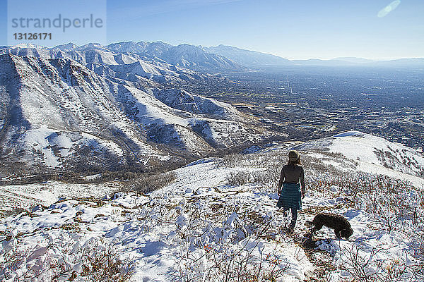 Hochwinkelaufnahme einer Frau mit Hund auf einem Berg im Winter