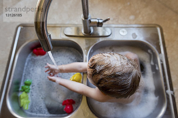 Hochwinkelaufnahme eines Jungen  der mit Wasser im Waschbecken spielt