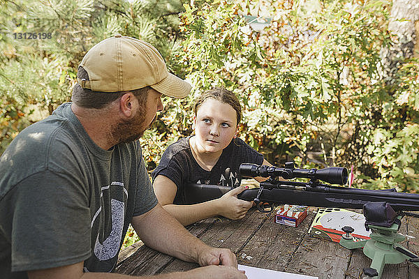 Hochwinkelansicht einer Tochter  die den Vater ansieht  während sie im Hinterhof das Gewehr hält