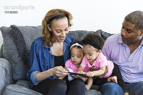 Eltern und Töchter schauen auf den Tablet-Computer  während sie auf dem Sofa sitzen