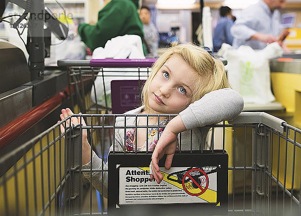 Gelangweiltes Mädchen mit Einkaufswagen im Supermarkt