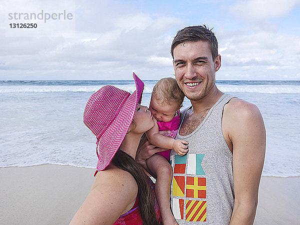 Glückliche Eltern mit süßer Tochter geniessen am Strand bei bewölktem Himmel
