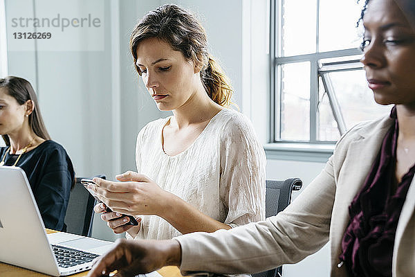 Geschäftsfrau benutzt Smartphone  während sie mit Kollegen im Büro sitzt