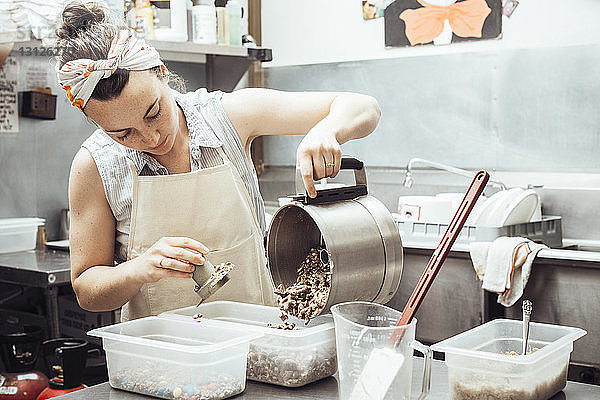 Frau gießt gemahlene Zutaten in einen Behälter  während sie in der Großküche Eiscreme zubereitet