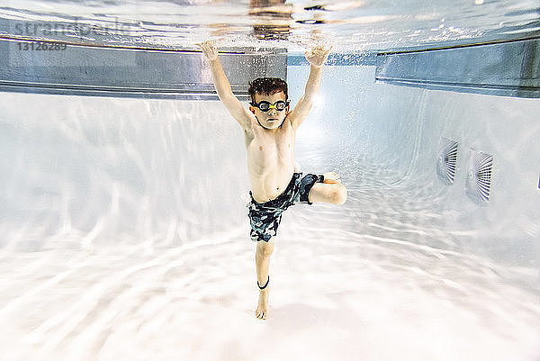 Junge ohne Hemd mit erhobenen Armen im Schwimmbad schwimmend