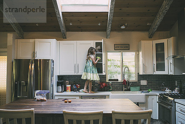Seitenansicht eines auf dem Küchentisch stehenden Mädchens