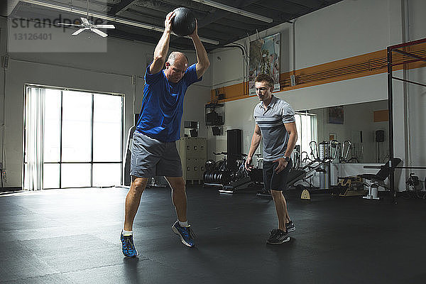 Trainer betrachtet Kunden  die im Fitness-Studio mit dem Fitnessball trainieren