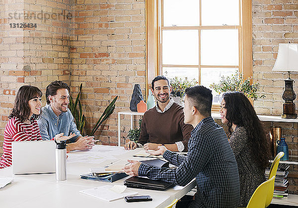 Glückliche Geschäftsleute sitzen während einer Besprechung im Büro am Schreibtisch