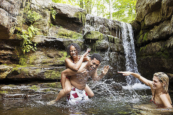 Fröhliche Freunde lachen und planschen im Fluss am Wasserfall