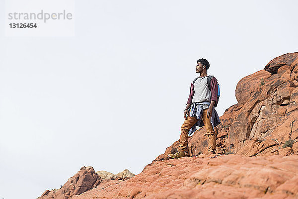Niedrigwinkel-Ansicht eines Mannes  der weg schaut  während er auf einer Felsformation vor klarem Himmel steht