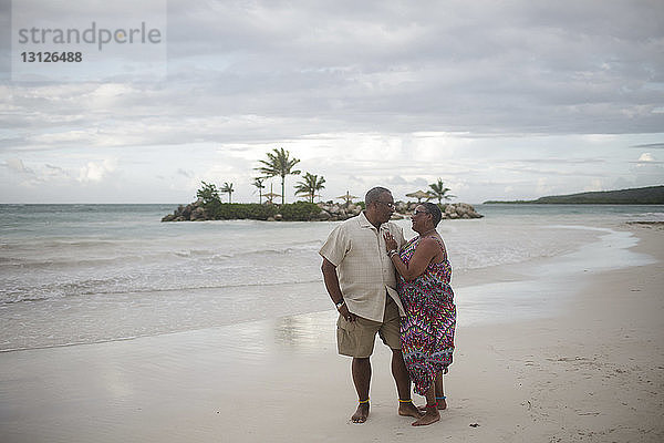 Älteres Ehepaar steht am Strand vor bewölktem Himmel