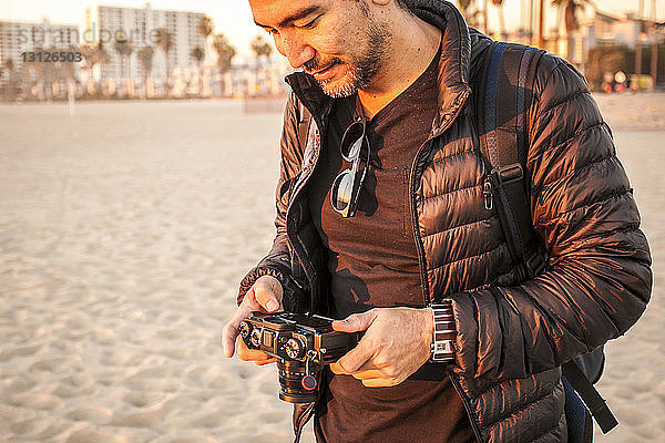 Mann trägt Jacke  während er am Strand eine Kamera hält