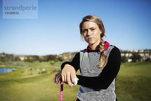 Porträt einer selbstbewussten Golfspielerin auf dem Feld vor klarem blauen Himmel