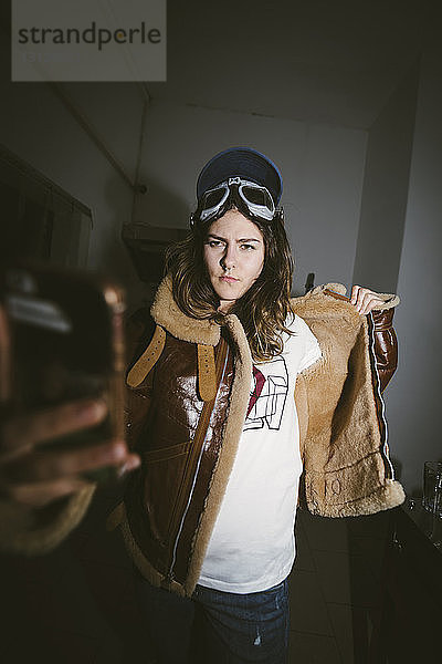 Selbstbewusste junge Frau mit Motorradbrille in Lederjacke beim Selbstversuch in der Dunkelkammer
