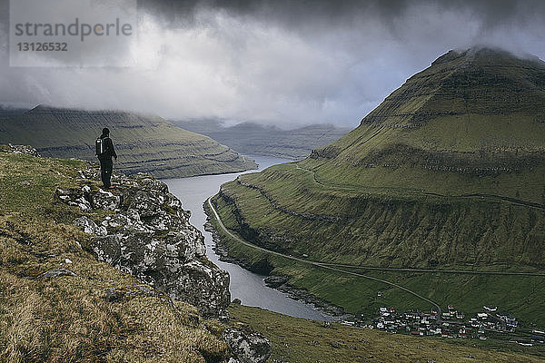 Wanderer schaut auf Aussicht  während er auf einer Klippe vor stürmischen Wolken steht