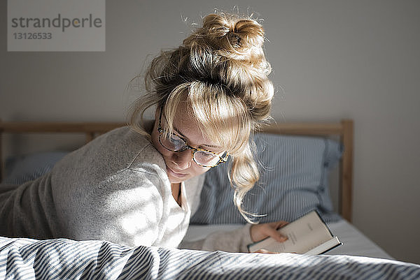 Seitenansicht einer Frau  die zu Hause auf dem Bett liegend ein Buch liest