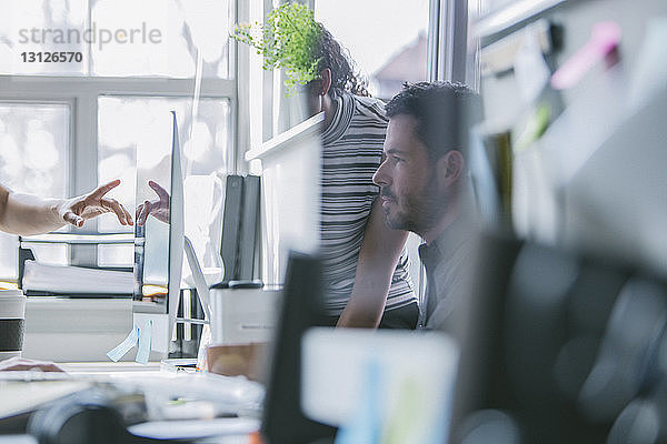 Geschäftsleute  die am Schreibtisch arbeiten und sich im Büro auf dem Computermonitor reflektieren