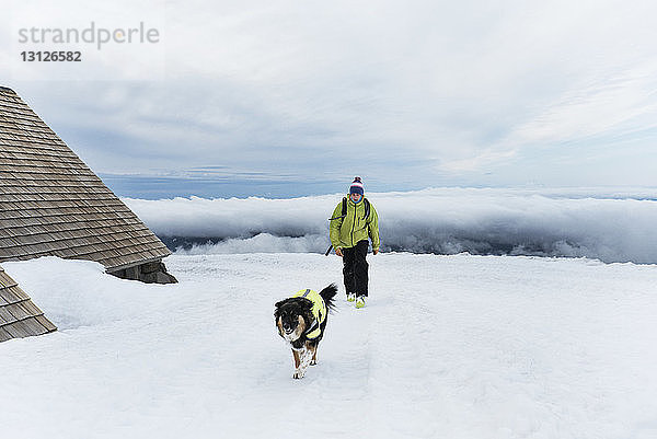 Mann geht mit Hund auf schneebedecktem Feld am Mount Hood gegen den Himmel