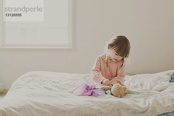 Mädchen spielt mit Teddybär auf dem Bett