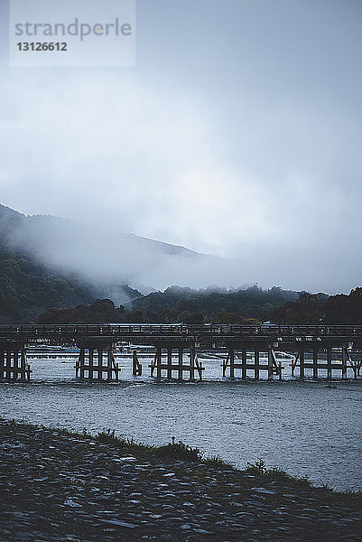 Brücke über den Fluss gegen den Himmel bei nebligem Wetter