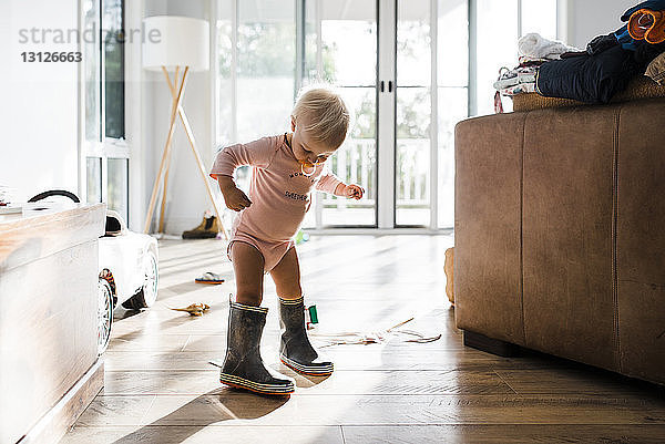 Kleinkind trägt Gummistiefel beim Schnullersaugen zu Hause