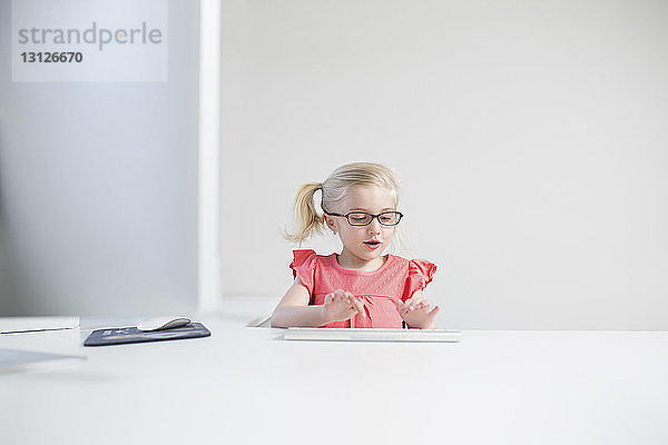 Glückliches Mädchen mit Brille beim Tippen auf der Tastatur am weißen Tisch