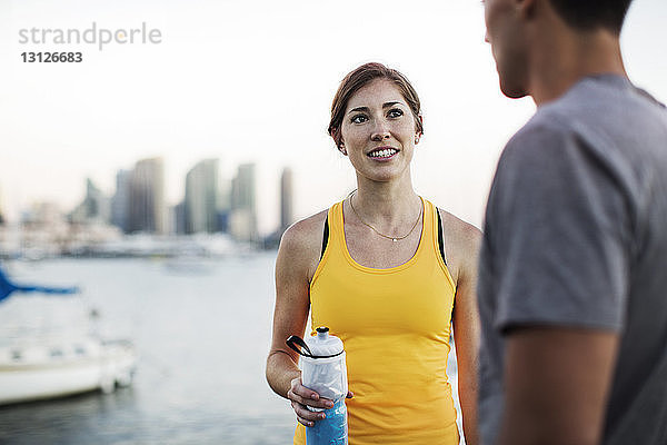 Sportliche Frau spricht mit Mann  während sie eine Wasserflasche am Hafen hält