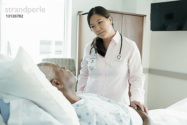 Ärztin betrachtet älteren Patienten  der auf der Krankenhausstation im Bett liegt