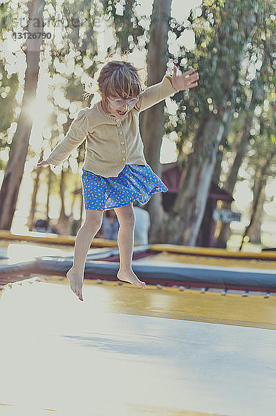 Mädchen springt auf dem Spielplatz in voller Länge auf dem Trampolin