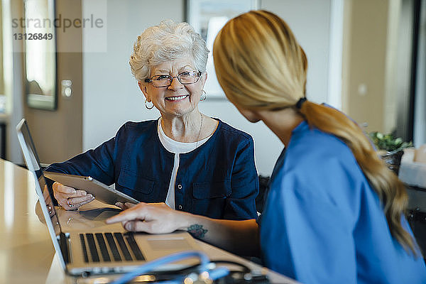Glückliche ältere Frau  die eine häusliche Pflegekraft ansieht  während sie einen Tablet-Computer hält