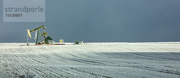 Panoramablick auf Pumpjack in der Ölindustrie auf Feld gegen Himmel im Winter