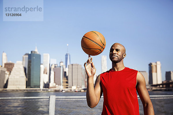 Lächelnder Mann dreht Basketball auf dem Finger gegen die Stadtsilhouette
