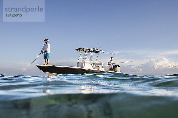 Tiefblick auf Männer  die fischen  während sie auf einem Boot auf See gegen den Himmel stehen