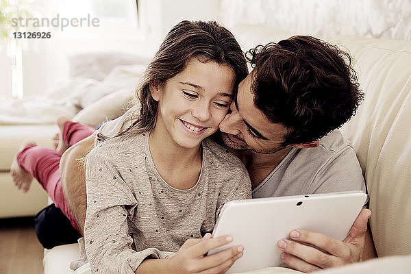 Vater umarmt Tochter mit digitalem Tablett  während er sich auf dem Sofa ausruht