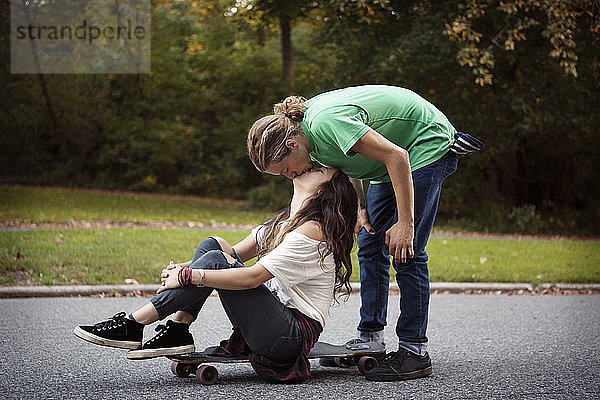 Mann küsst Frau  die auf einem Skateboard auf der Straße sitzt