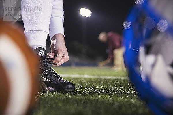 Unterer Teil eines American-Football-Spielers beim Schnürsenkelbinden auf dem Spielfeld mit dem Trainer im Hintergrund