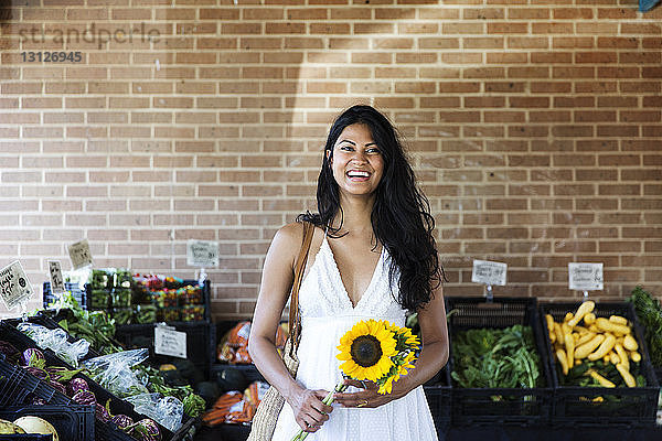 Glückliche Frau hält Sonnenblumen  während sie auf dem Markt steht