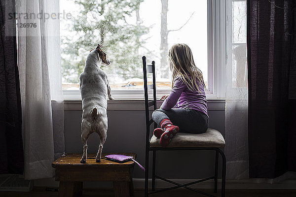 Mädchen in voller Länge mit Hund zu Hause am Fenster sitzend