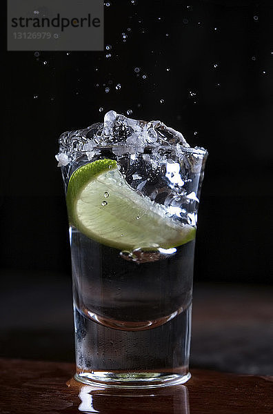 Nahaufnahme einer Limettenscheibe in Tequila auf Holztisch vor schwarzem Hintergrund
