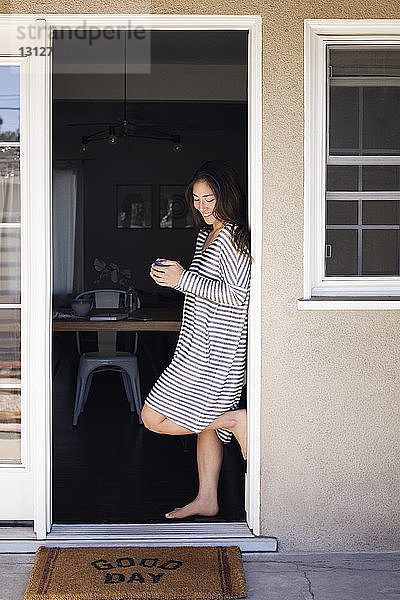 Glückliche Frau hält Kaffeetasse  während sie an der Tür steht