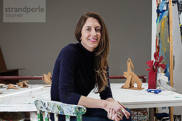 Porträt einer glücklichen Künstlerin  die am Tisch im Kunstatelier sitzt
