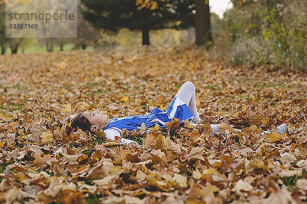 Mädchen entspannt sich auf einem mit Herbstlaub bedeckten Feld im Park