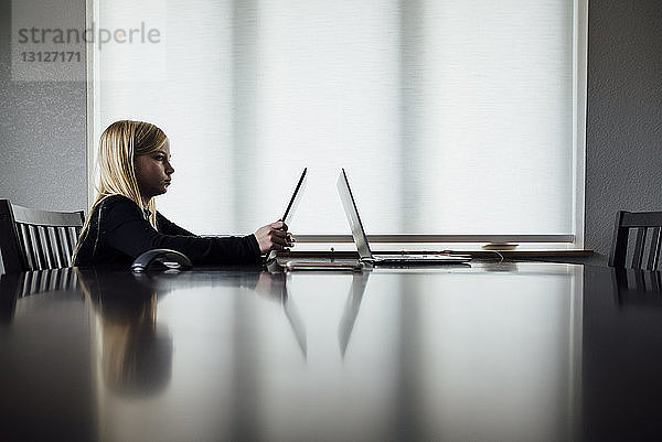 Seitenansicht eines Mädchens  das einen Laptop-Computer benutzt  während es zu Hause sitzt