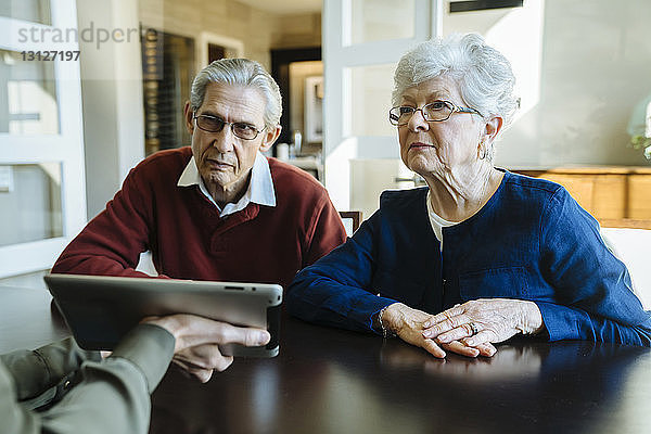 Ausgeschnittenes Bild eines Finanzberaters  der einem älteren Ehepaar den Plan auf einem Tablet-Computer im Büro erklärt
